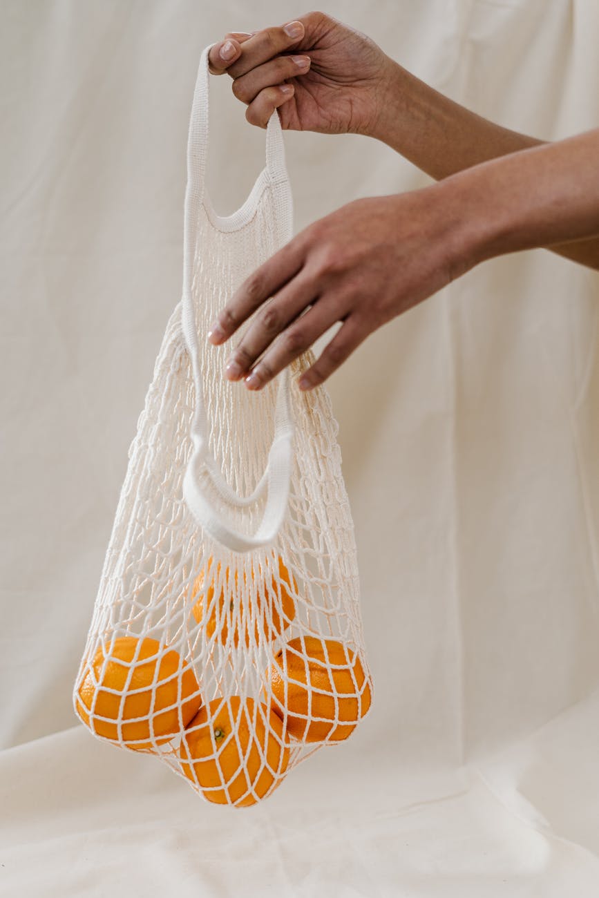 person holding four oranges in white net bag