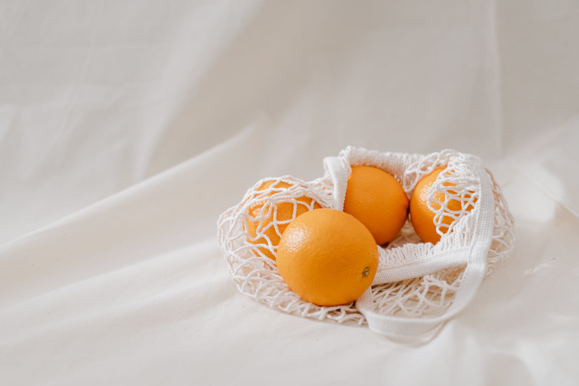 four orange fruits in a basket on white linen