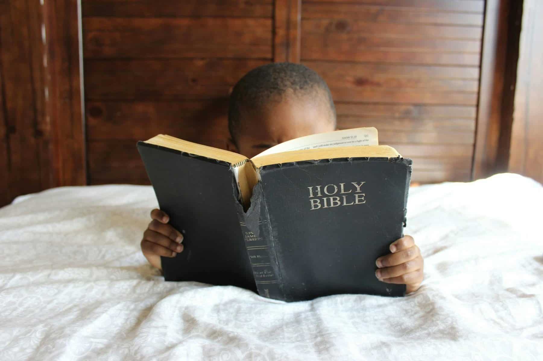 Young child reading a Holy Bible indoors, conveying a serene and religious atmosphere. | short bible verses for kids